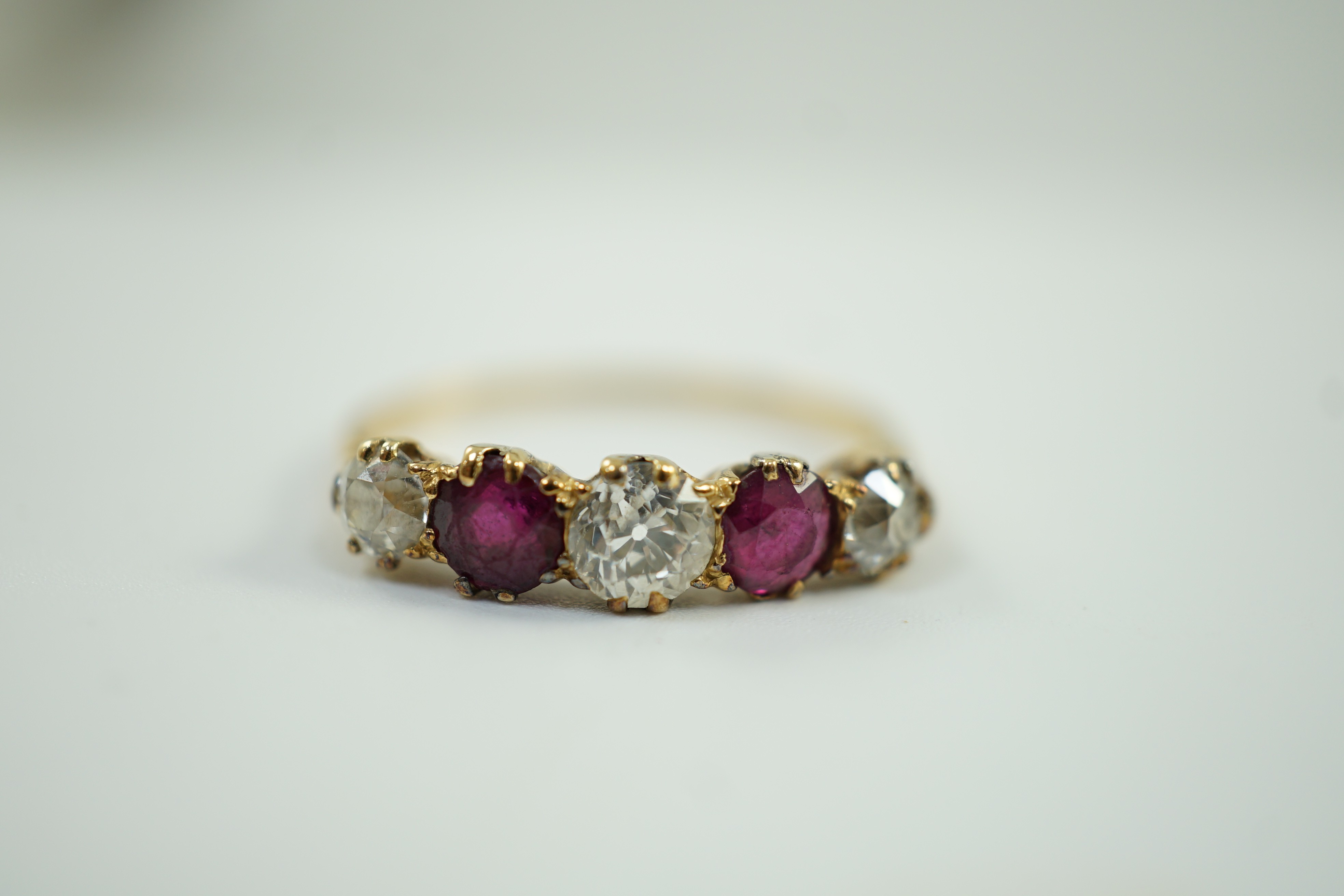A yellow metal, three stone diamond and two stone ruby set half hoop ring, size V, gross weight 3.2 grams.